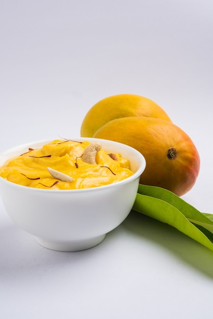 Amrakhand ist ein Joghurt mit Alphonso-Geschmack oder Shrikhand, eine beliebte indische Süßigkeit, die mit Trockenfrüchten und Safran mit ganzen Mangofrüchten auf buntem Hintergrund serviert wird. selektiver Fokus