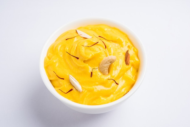 Amrakhand ist ein Joghurt mit Alphonso-Geschmack oder Shrikhand, eine beliebte indische Süßigkeit, die mit Trockenfrüchten und Safran mit ganzen Mangofrüchten auf buntem Hintergrund serviert wird. selektiver Fokus