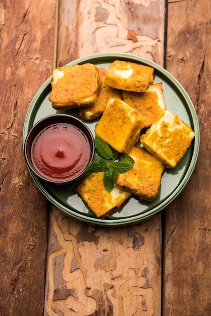 Amritsari Paneer Tikka hecho con cubos de requesón bañados en una masa hecha con besan, chat masala y especias y frito poco profundo en una sartén, servido con salsa de tomate