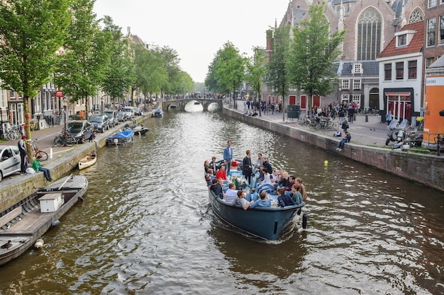 AMSTERDÃ, PAÍSES BAIXOS, 01 DE JUNHO DE 2016: Vista de um dos canais e barcos com jovens e um prédio antigo ao fundo em Amsterdã, Holanda Eon 01 de junho de 2016.