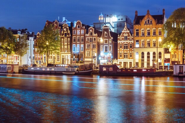 Amsterdamer Kanal amstel mit typisch holländischen Häusern Hausboot und leuchtender Spur vom Boot bei Nacht