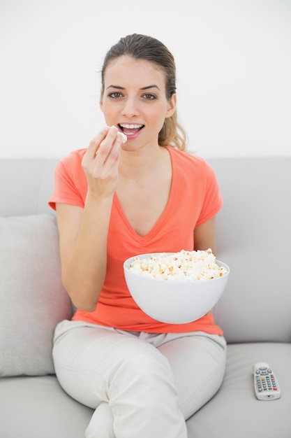 Amusada jovem assistindo televisão com pipoca