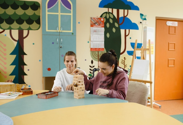 An einem großen Tisch sitzen zwei Mädchen mit Behinderungen und spielen Jenga