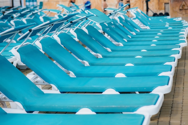 An einem sonnigen Tag stehen viele neue schöne blaue Sonnenliegen in der Nähe des Pools im Hotel. Schöne Ferien. Sommerferien und Tourismus.