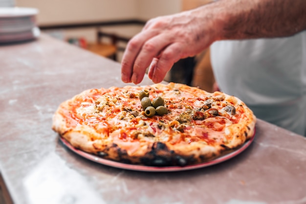 Añadiendo el toque final. Chef poner aceitunas en una pizza. De cerca.