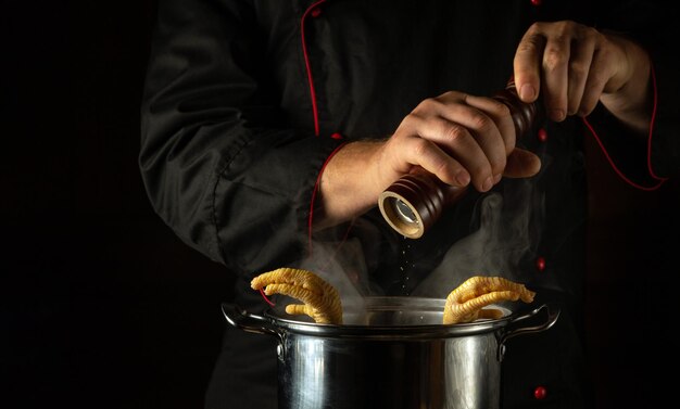 Foto añadir pimienta seca con las manos del cocinero a una sartén de patas de pollo hirviendo el concepto de preparar un plato de acompañamiento o sopa rica en la cocina de un restaurante o hotel