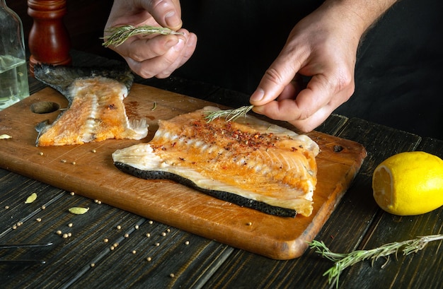 Añadir romero a los filetes de pescado para el aroma y el sabor de la cocina asiática El proceso de preparación de pescado por las manos de un chef en la cocina de un restaurante