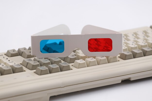 Anaglyph 3D-Brille auf alter PC-Tastatur. Weißer Hintergrund. Retro-Attribute der 80er Jahre