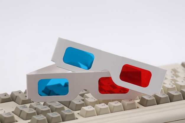 Anaglyph 3D-Brille auf alter PC-Tastatur. Weißer Hintergrund. Retro-Attribute der 80er Jahre
