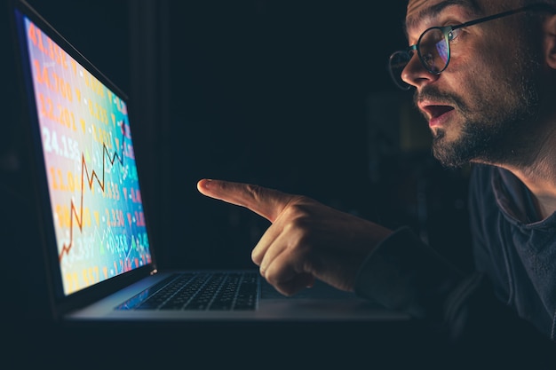 Analista de comerciante de homem de negócios sério olhando para um monitor de computador, corretor de investidores, analisando índices, gráfico financeiro, negociando dados de investimento on-line no gráfico do mercado de ações criptomoeda na tela do pc.