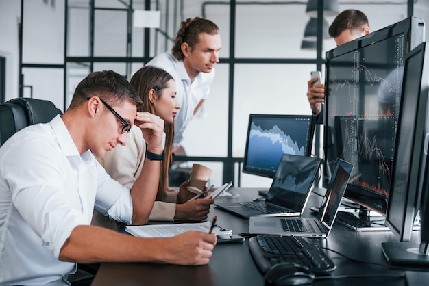 Analizando información El equipo de corredores de bolsa trabaja en una oficina moderna con muchas pantallas