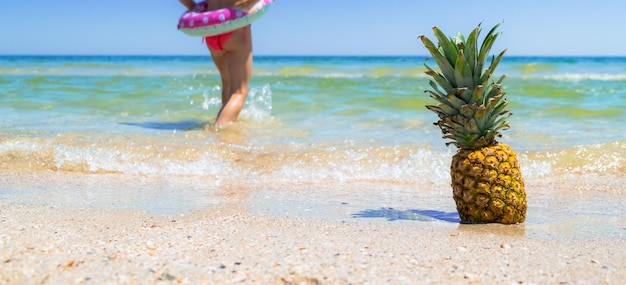 Ananas am Strand mit Kind, das ins Wasser geht, Meeresananasfrucht