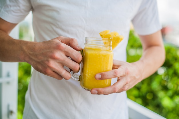 Ananas-Cocktail mit einer Scheibe in den Händen Mann auf der Terrasse. Tropisches Konzept