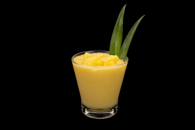 Ananas-Mango-Smoothie im klaren Glas mit Ananasblättern und Ananaswürfeln.