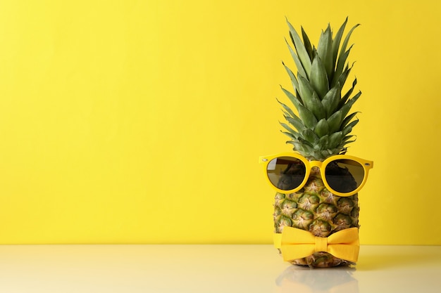 Ananas mit Krawattenschleife und Sonnenbrille gegen gelben Hintergrund