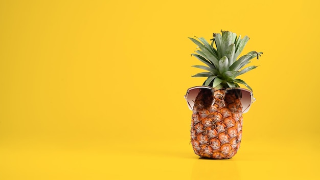 Ananas mit Sonnenbrille vor gelbem Hintergrund mit Kopierbereich Strand und tropisches Thema