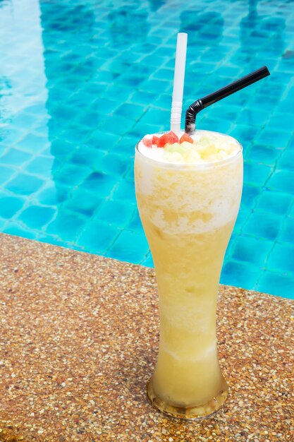 Ananas Smoothie im hohen Glas mit Swimmingpoolhintergrund.