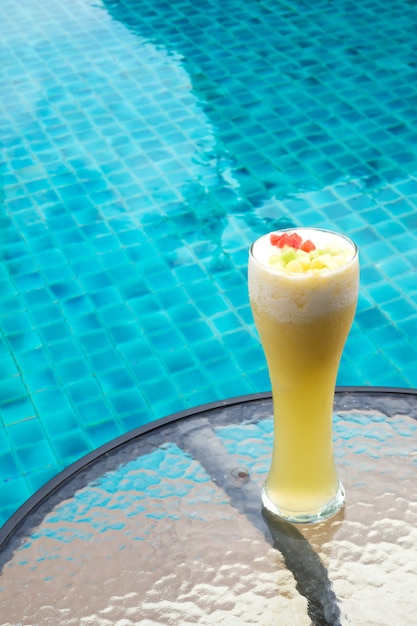 Ananas Smoothie im hohen Glas mit Swimmingpoolhintergrund.