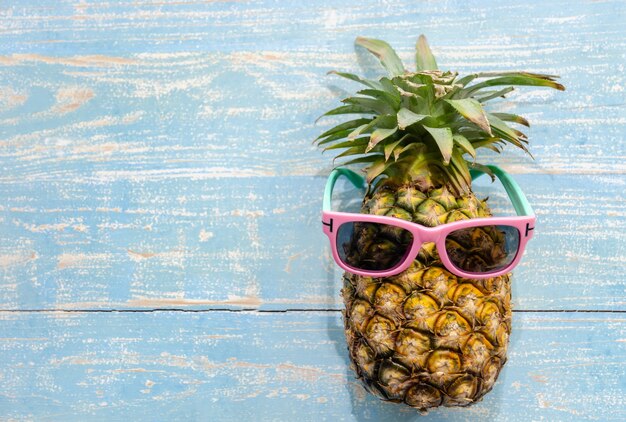 Ananas tropische Frucht mit rosa Sonnenbrille auf blau verwitterter Holzoberfläche