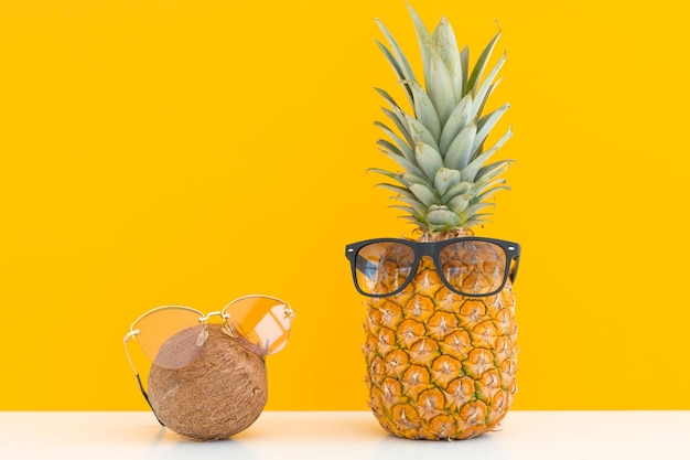 Ananas und Kokosnuss mit Sonnenbrille ruhen und Cocktail am Strand trinken Sommerurlaub