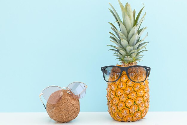 Ananas und Kokosnuss mit Sonnenbrille ruhen und Cocktail am Strand trinken Sommerurlaub