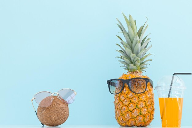 Ananas und Kokosnuss mit Sonnenbrille ruhen und Cocktail am Strand trinken Sommerurlaub