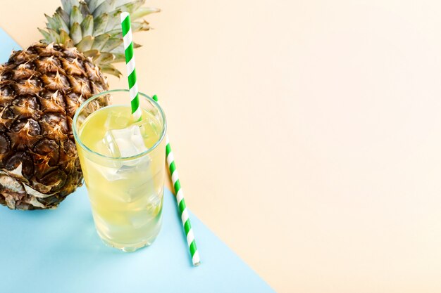 Ananas und Saft mit Eis in einem Glas, auf einer blauen gelben Sommerstimmung, Kopienraum.