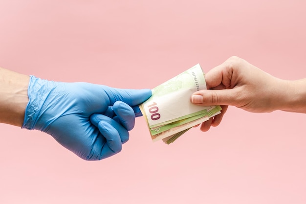 Anbieten von Geld Griwna an eine Hand in blauer OP-Handschuh-Krankenschwester oder Arzt Korruption