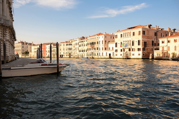 Un ancho canal en la Venecia italiana entre edificios antiguos, iluminado por el sol, con barcos en él.