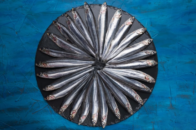Anchovas na forma de um círculo em uma pedra preta. Frutos do mar. Peixe pequeno mar