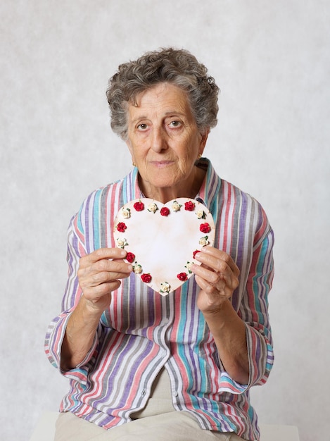 La anciana de entre 70 y 80 años mantiene el corazón en las manos. fondo gris