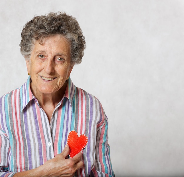 La anciana de entre 70 y 80 años mantiene el corazón en las manos. fondo gris