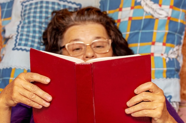 Una anciana se acuesta en el sofá y lee un libro.