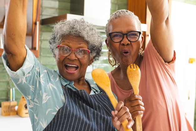 Una anciana afroamericana y una anciana biracial celebran con utensilios de cocina