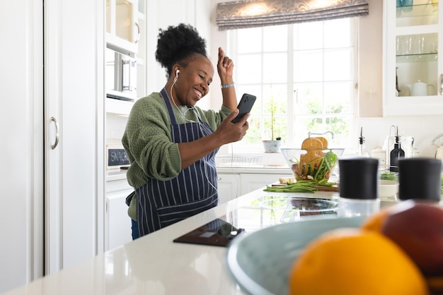 Una anciana afroamericana feliz escuchando música y haciendo ensalada en la cocina de su casa.