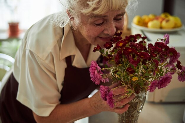 Anciana alegre oliendo flores en casa