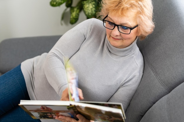 Una anciana alegre sosteniendo un álbum de fotos familiar sentada en un sofá en casa, una anciana viendo un fotolibro