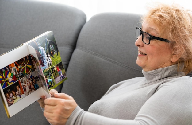 Una anciana alegre sosteniendo un álbum de fotos familiar sentada en un sofá en casa, una anciana viendo un fotolibro