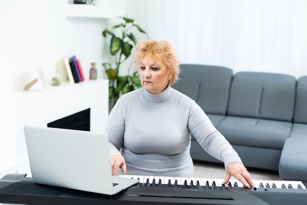 anciana aprendiendo a tocar sintetizador en una laptop en línea en casa.