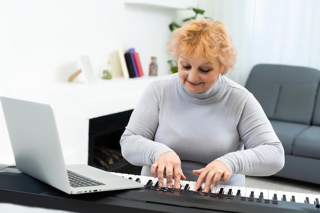 anciana aprendiendo a tocar sintetizador en una laptop en línea en casa.