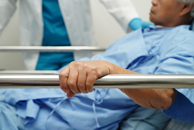 Anciana asiática anciana paciente sosteniendo barandilla de la cama mientras se acuesta con esperanza esperando a su familia en el hospital