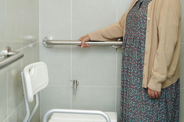 La anciana asiática anciana utiliza el riel de soporte del inodoro en el pasamanos del baño, la seguridad de la barra de seguridad en el hospital de enfermería