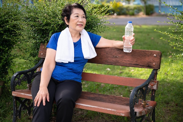 Anciana asiática cansada y descansa con toalla y agua pura en botella de plástico después de trotar