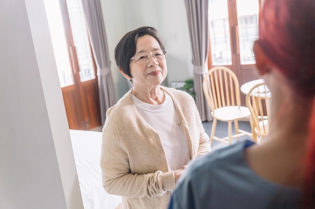 Una anciana asiática da la bienvenida a una enfermera asiática que lleva una visita de cuidador a domicilio en la entrada con una sonrisa y una pequeña charla Concepto de cuidado de la salud en el hogar y hogar de ancianos