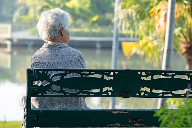 Anciana asiática deprimida y triste sentada en un banco en el parque de otoño