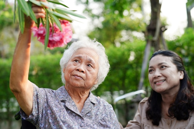 Anciana asiática disfruta en un jardín de flores con un cuidador en el parque