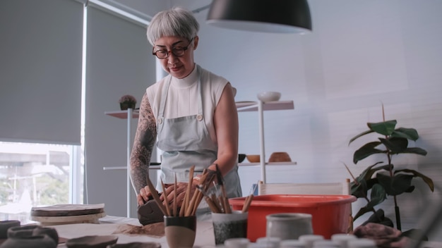 Una anciana asiática disfruta del trabajo de alfarería en casa Una ceramista está haciendo nueva alfarería en un estudio