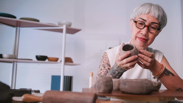 Una anciana asiática disfruta del trabajo de alfarería en casa Una ceramista está haciendo nueva alfarería en un estudio