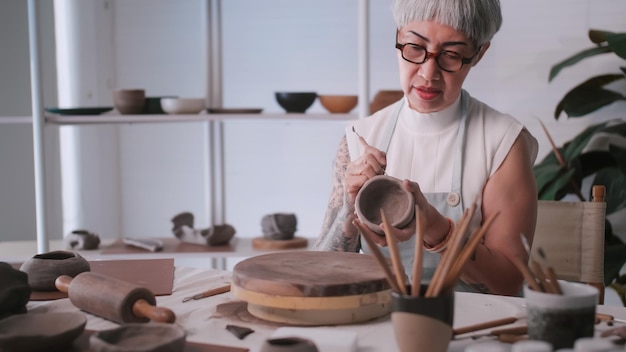 Una anciana asiática disfruta del trabajo de alfarería en casa Una ceramista está haciendo nueva alfarería en un estudio