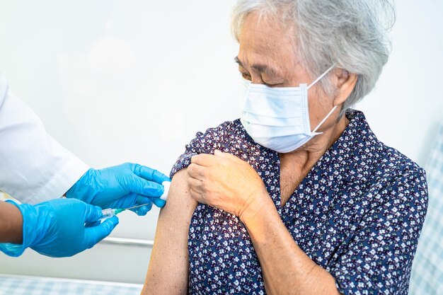 Anciana asiática de edad avanzada con mascarilla facial que recibe la vacuna covid19 o coronavirus por parte de un médico que se inyecta